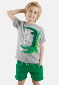 Harmaa puuvillapaita, jossa on vihreä krokotiilikuva ja valkoiset sanat "CROCODILE". Yhdistetty vihreisiin shortseihin.
