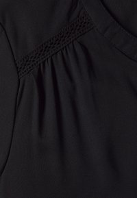 Haut en tissu noir avec des plis et un détail décoratif en dentelle le long du décolleté. Le matériau est lisse et léger.