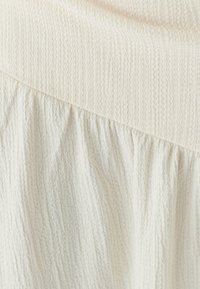 Le tissu couleur crème présente une couture texturée en haut, se transformant en une couche plissée et plus douce en dessous.