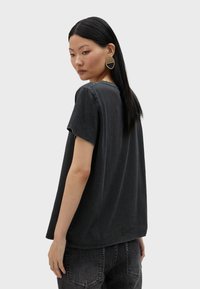 Camiseta de algodón negra con mangas cortas y escote redondo, con un corte relajado y detalles sutiles de desgaste. Combinada con jeans oscuros.