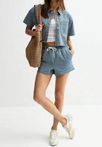 Camicia di denim a maniche corte, canotta bianca, pantaloni corti a righe e sneaker beige. Borsa intrecciata appoggiata sulla spalla; outfit casual.