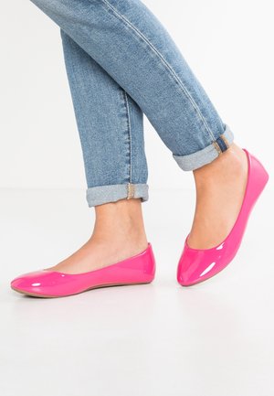 Jasnoróżowe, lakierowane baletki z okrągłym noskiem i minimalistycznym designem, noszone z podwiniętymi niebieskimi dżinsami.