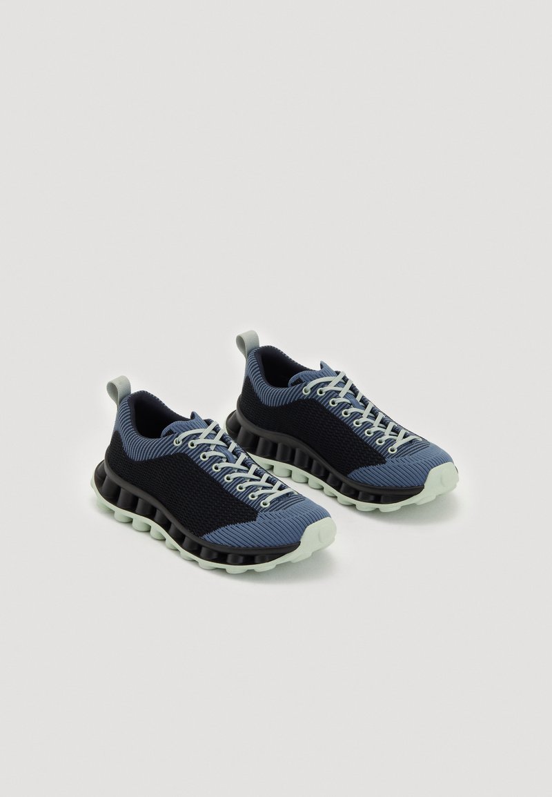 Blaue und schwarze Sportschuhe mit einem strukturierten Obermaterial, weißen Schnürsenkeln und einer übertriebenen schwarzen Sohle mit abgerundeten Akzenten. Leichtes Design.