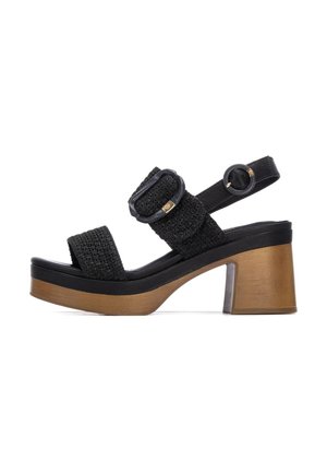 Sandalia de tela negra tejida con dos hebillas ajustables, tacón grueso de madera y suela de goma; diseño de punta abierta, correa plana en el tobillo.