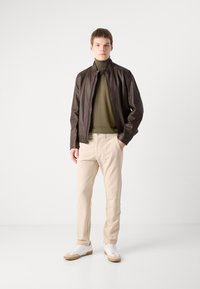 Brown leather jacket over an olive green turtleneck, paired with beige trousers and white sneakers with brown accents. Smooth texture and tailored fit.