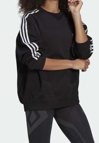 Svart sweatshirt i mjukt tyg med vit tre-stripsdesign på ärmarna och en klassisk rund halsringning. Avslappnad passform.