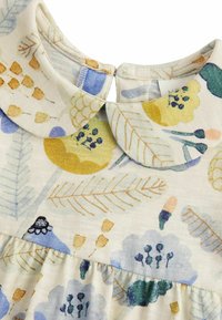 Vestido infantil con cuello redondeado, que presenta un patrón floral y de hojas en tonos pastel de amarillo, azul, verde y marrón sobre fondo crema.