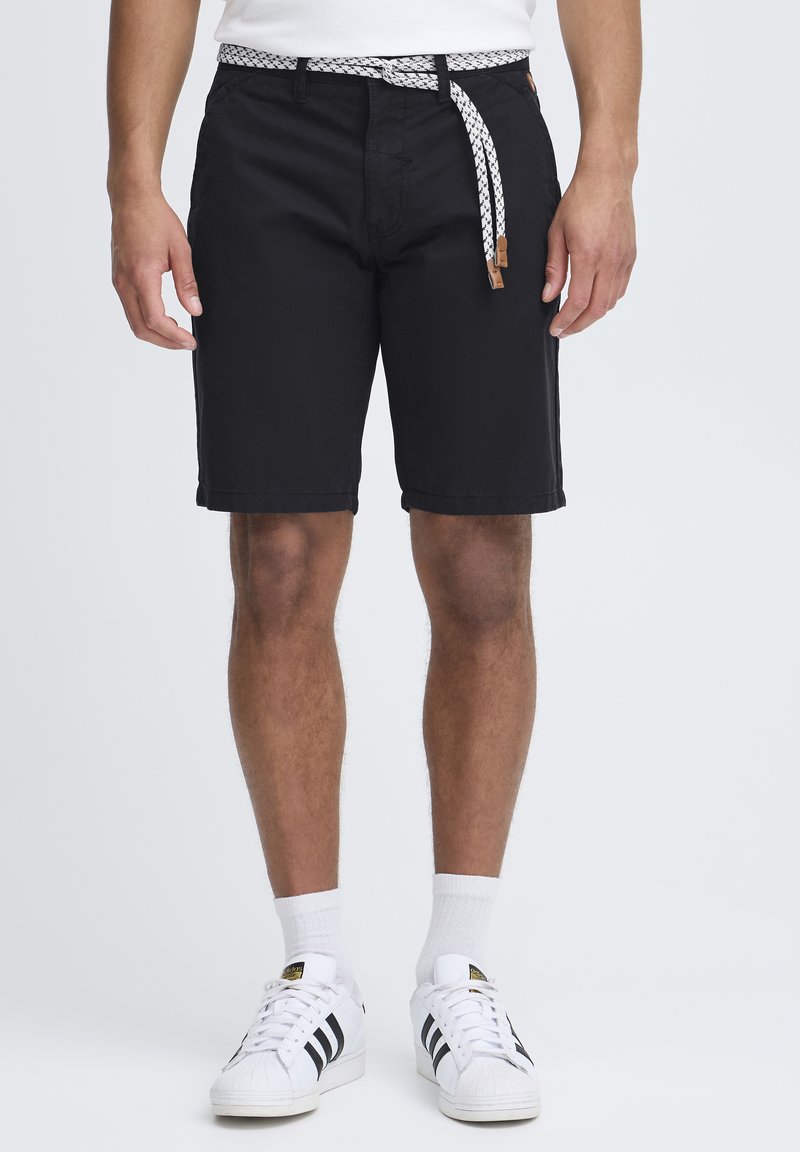 Shorts noirs en coton, avec une ceinture à motif blanc, des poches avant et une coupe droite. Portés avec des baskets blanches et des chaussettes.