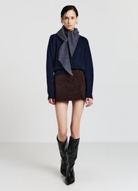 Maglione blu navy e sciarpa grigia, mini gonna in velluto a coste marrone e stivali neri al ginocchio. Texture lisce con forme sovrapposte e rilassate.