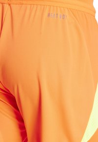 Oranje sportbroekjes gemaakt van lichtgewicht, vochtregulerende stof, met een HEAT.RDY-logo in paars. Inclusief een meshpaneel voor ademend vermogen.