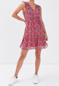 Red floral dress with ruffled sleeves, V-neckline, and tiered skirt. Worn with white sneakers. Light, flowing fabric with a delicate pattern.