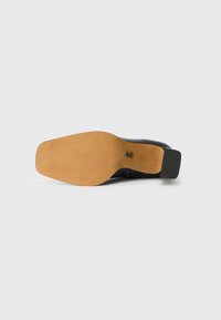 Black shoe sole with a light brown rubber base. Smooth texture with a ribbed pattern for grip. Features a small black accent on the heel.