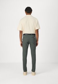 Beżowa koszulka polo z krótkim rękawem noszona z ciemnozielonymi dopasowanymi spodniami i czarnym paskiem, uzupełniona o jasnobeżowe buty. Minimalistyczny design.