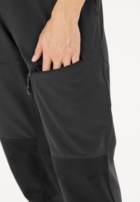 Zwarte sportbroek met een ritszak aan de zijkant en een getextureerde grip trekhaak. Glad stof met tonale paneeldetails.