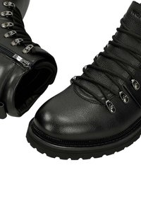 Stivali da trekking in pelle nera caratterizzati da materiale testurizzato, hardware argentato, chiusura con zip e una suola in gomma resistente con una punta ampia.