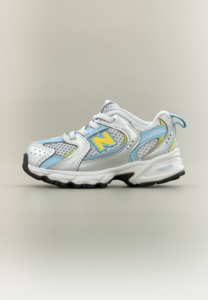 Fehér és világoskék New Balance 530 tornacipő sárga részletekkel, hálós panelek és fekete talprészel, oldalnézet.