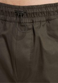 Donkerbruine shorts met een elastische tailleband en verstelbare trekkoord, voorzien van een zijzak en een gladde stoftextuur.