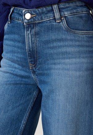 Jeans in denim blu con un taglio aderente, dotati di chiusura a bottone argentato, cuciture evidenti e una leggera scoloritura sulla trama del tessuto.