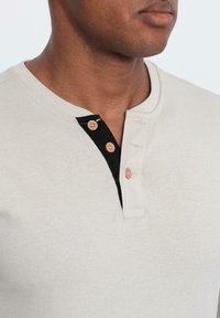 Korte mouwen henley-shirt in lichtbeige met een zwarte placket die drie beige knopen heeft en van een gestructureerde stof is gemaakt.