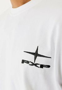 T-shirt bianco in cotone con scollatura a girocollo e logo ricamato nero che presenta una stella e le lettere "PXP" nella zona sinistra del petto.