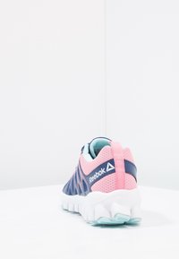 Reebok-sneakers med ett mesh-övre i rosa och marinblått, vit mellansula, turkosa accenter och en kontrasterande dragflik vid hälen.
