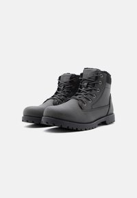 Crne čizme do gležnja od sintetičkog materijala, sa vezanjem, podstavljenim ovratnikom i čvrstim gumiranim potplatom s dubokim reljefom.