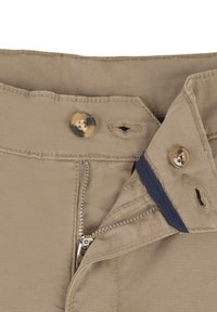 Pantalons beiges avec une fermeture éclair en métal, des boutons dorés et un accent bleu à la taille. Gros plan sur la taille et les détails de fermeture.