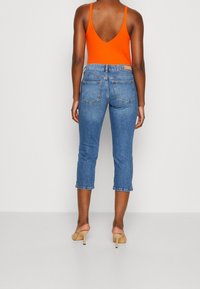 Orange ärmlös bodysuit som kombineras med korta blå denimjeans. Jeansen har en klassisk femfickorsdesign och uppvikta fållar.