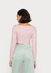 Top crop de mangas longas lilás claro, com pequeno padrão floral em amarelo e laranja. Tecido suave com decote arredondado e desenho ajustado.