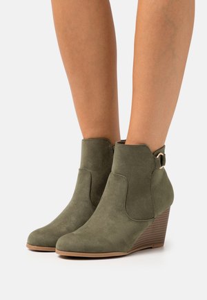 Bottines en daim vertes à talon compensé, avec une découpe sur le côté et une finition décorative en boucle. Texture lisse et design à bout rond.