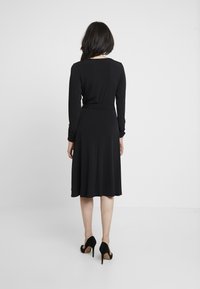 Svart långärmad klänning med en figursydd bodice och en utställd midiklänning, gjord av mjukt tyg, med en minimal design.