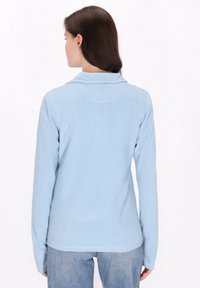 Sudadera de felpa azul clara con mangas largas y cuello desdoblado. Textura suave y detalles de costura mínimos. Combinada con jeans azul claros.