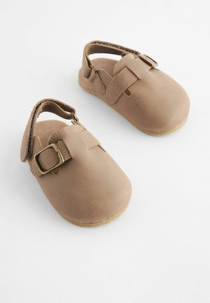 Chaussures en cuir marron avec un bout rond et une bride à boucle. Le design comprend un talon ouvert et une semelle en caoutchouc texturée.