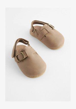 Pantofi din piele maro cu vârf rotund și o curea cu cataramă. Designul include un călcâi deschis și o talpă texturată din cauciuc.