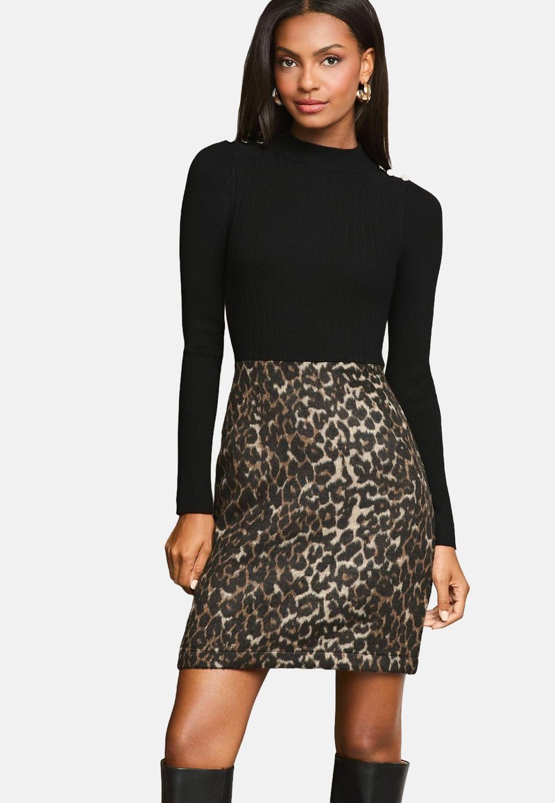 Top tricotat negru cu guler înalt, asortat cu o fustă cu imprimeu leopard. Detaliu notabil: accente cu nasturi pe umăr. Textură netedă în ansamblu.