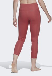 Punaiset capri-leggingsit, jotka on valmistettu joustavasta kankaasta. Niissä on korkea vyötärö, sileä pinta ja pieni logo alhaalla lahkeessa.