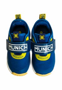 Sneaker blu con cinturino in velcro, dettagli gialli e branding "MUNICH". Parte superiore in tessuto morbido e suola in gomma con una texture particolare.