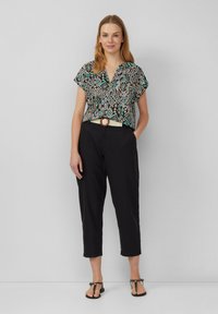 Zwart-wit gestreepte top met korte mouwen, gecombineerd met zwarte taps toelopende broeken en een geweven crème riem. Zwarte platte sandalen maken de look compleet.