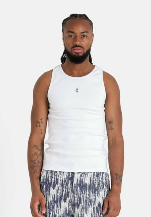 Camiseta sin mangas blanca de canalé con un escote redondo, que presenta un pequeño logotipo azul. Combinada con pantalones cortos ligeros y con estampado en azul oscuro y blanco.