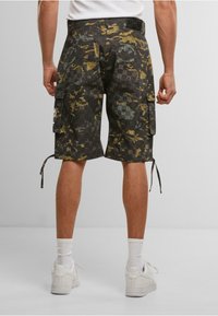 Cargo shorts in dark camouflage pattern featuring green, yellow, and gray accents. Includes side pockets and adjustable drawstrings at the hem.
