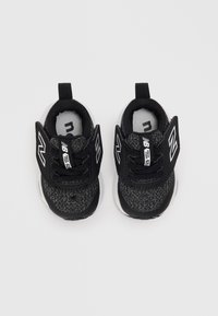 Baskets de sport noires avec un haut en tissu texturé, présentant des accents en mesh, une semelle blanche et un logo bien visible sur le côté et la languette.