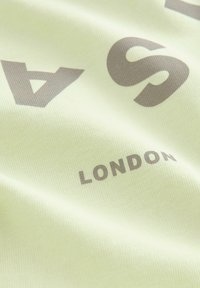 Svetlozelená látka s hladkou textúrou, na ktorej sú veľké, tmavošedé písmená a slovo "LONDON" v menšom písmene.