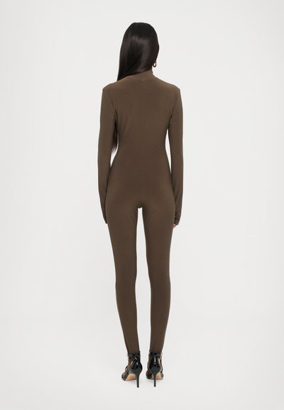 Brown long-sleeve jumpsuit with a fitted silhouette. Smooth texture, round neckline, and slim legs, complemented by black high-heeled shoes.