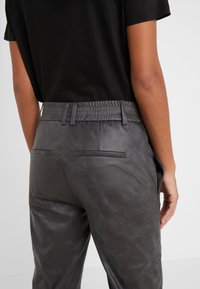 Zwarte faux leren broeken met een elastische tailleband, achterzakken en een gladde textuur, met een matte afwerking.