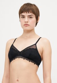 Bralette en dentelle noire avec un haut en mesh, présentant un décolleté en V et des bords festonnés. Les bretelles sont fines et ajustables pour un meilleur ajustement.