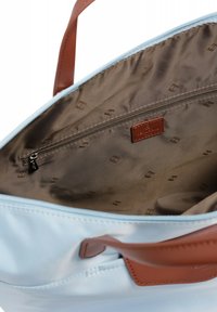 Interno di una borsa tote blu in nylon con foderatura in tessuto marrone, tasca con zip e etichetta con logo. Tessuto morbido con dettagli di cucitura a contrasto.