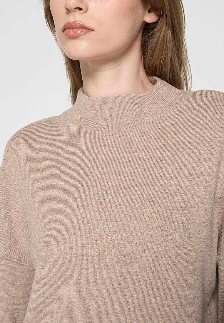 Beige Strickpullover mit hohem Kragen, gerippter Struktur und lässiger Passform. Weiches Material mit dezenten Farbvariationen.