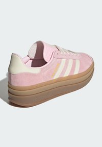 Ružové semišové tenisky s bielymi akcentmi, s textúrovanou podrážkou a vrstveným platformovým dizajnom. Logo "Gazelle" v žltej farbe na boku.