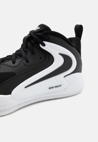 Scarpa sportiva nera realizzata in materiale mesh e sintetico, design elegante, accento curvo bianco e la scritta "JUST DO IT" stampata sulla suola.