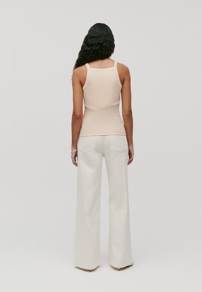 Canotta aderente color beige chiaro con spalline sottili e superficie liscia, abbinata a pantaloni bianchi a vita alta e gamba ampia con tasche posteriori.